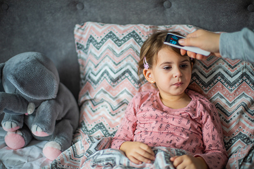 Caring mother measuring her daughter temperature with digital thermometer