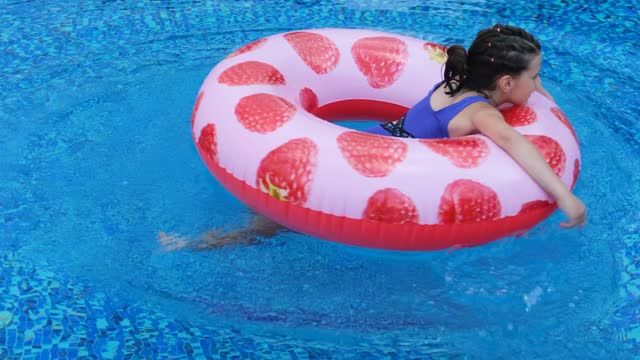 Girl child swims in an outdoor pool on a red inflatable circle
