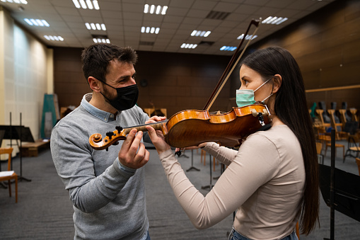 Rear view of a violin teacher speaking to a woman student and explaining how to hold a violin