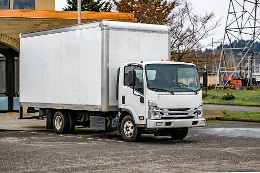 La cabina sobre un semirremolque compacto blanco con remolque de caja larga entrega la carga a las empresas locales y descarga las mercancías que se encuentran en el estacionamiento photo