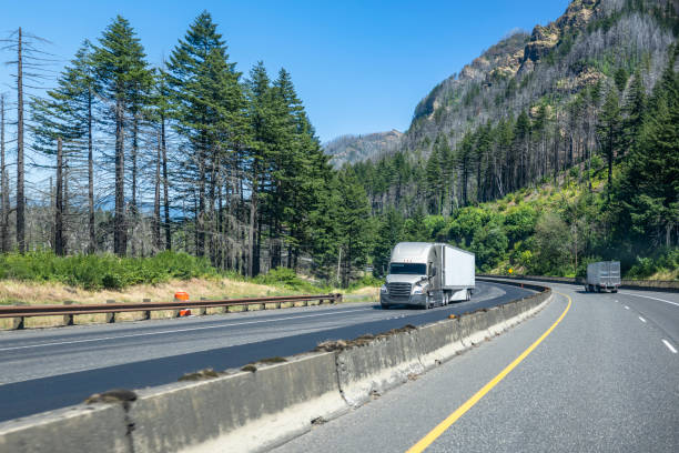 istock Two big rig semi trucks with refrigerator semi trailers running in opposite directions on the divided highway road with rock mountains and green trees on the sides 1910625677