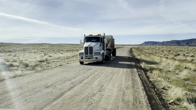 Handheld Shot of a White Semi Truck Pulling a Dump Trailer on Dirt Road in the Utah Desert on a Sunny Winter Day