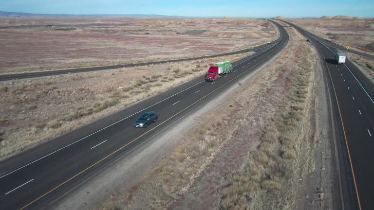 A Drone Shot of a Semi Truck with a Flatbed Trailer Loaded with Supplies on a Two Lane Interstate on a Sunny Winter Day