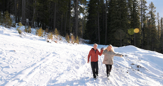 Mature couple enjoy winter walk through forest together