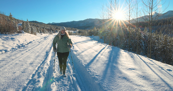 Mature woman walks down snowy track through forest on sunny day