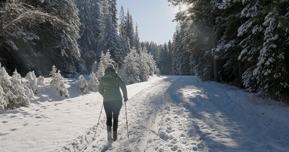 Mature woman walks down snowy track through forest on sunny day