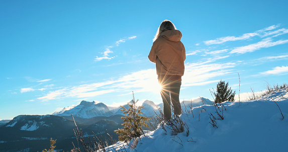 Young woman explores snowy hillside above mountains on sunny day