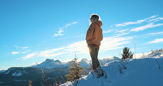 Young woman explores snowy hillside above mountains on sunny day