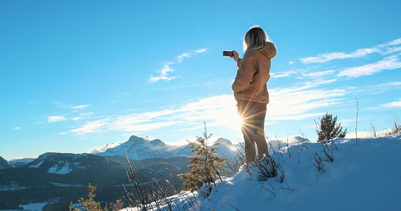 Young woman explores snowy hillside above mountains on sunny day
