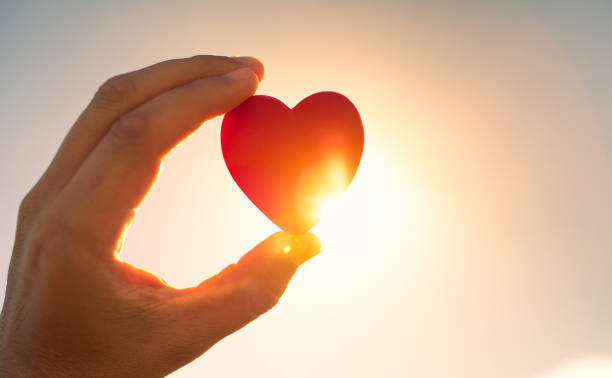 istock Hand showing red heart against a sunset. 1910855367