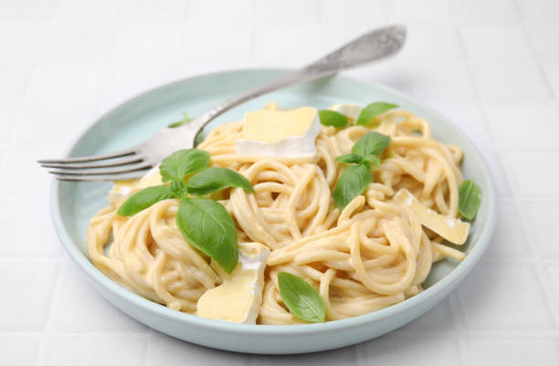 istock Delicious pasta with brie cheese, basil and fork on white tiled table, closeup 1910861052