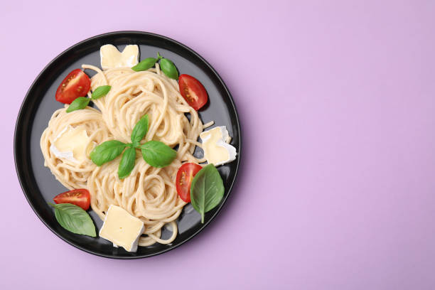 istock Delicious pasta with brie cheese, tomatoes and basil leaves on violet background, top view. Space for text 1910861570