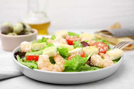 Delicious Caesar salad with shrimps on light table, closeup