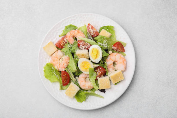 istock Delicious Caesar salad with shrimps on light table, top view 1910863653