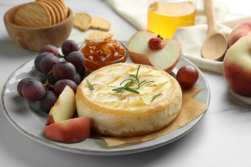 Tasty baked brie cheese with fruits and jam on white marble table, closeup