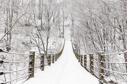 Snow-covered, pedestrian bridge over a ravine in the winter forest. Lots of snow on a beautiful road towards the forest.