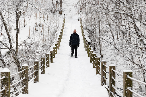 A hiker enjoying winter snowshoeing crossing a snow covered suspension bridge in a white forest.