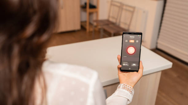 istock Woman in home kitchen using phone app to remotely control lighting system 1910887480