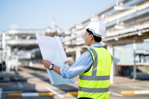istock Engineer Electrician holding blueprints looking confident with a factory plant background, contractor inspection constructed on-site, Solar power station site and architecture concept. 1910902970