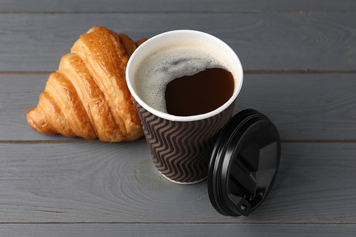 Coffee to go. Paper cup with tasty drink and croissant on grey wooden table