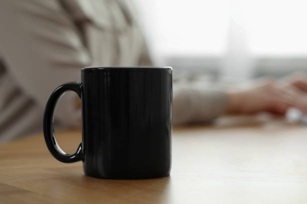 istock Black ceramic mug on wooden table. Woman at workplace, selective focus. Space for text 1910916968