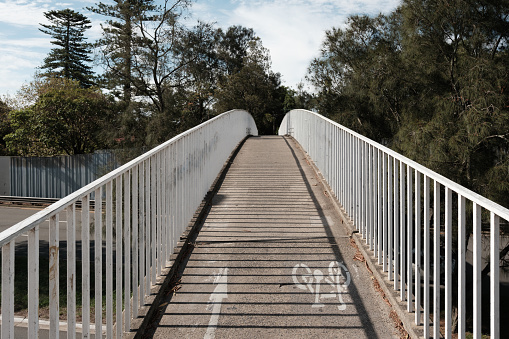 Concrete pedestrian footbridge with white metal handrail and trees beyond.