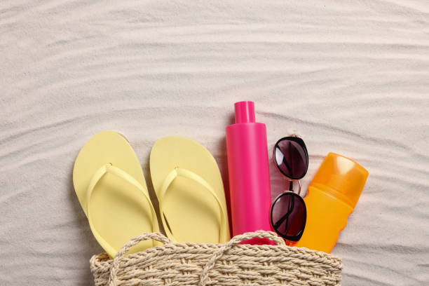 istock Wicker beach bag with sunscreen, flip flops and sunglasses on sand, flat lay 1911019377