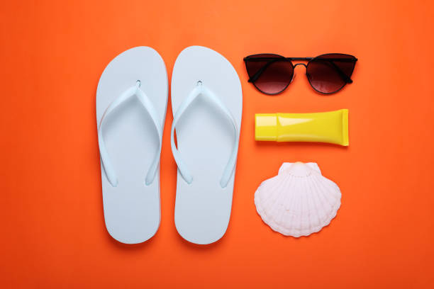 istock Stylish white flip flops, sunglasses, sunscreen and seashell on orange background, flat lay 1911022569