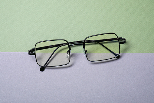 Stylish pair of glasses with black frame on color background, top view