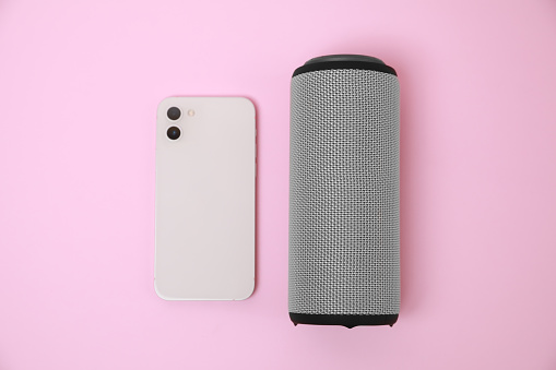 Portable bluetooth speaker and smartphone on pink background, flat lay. Audio equipment