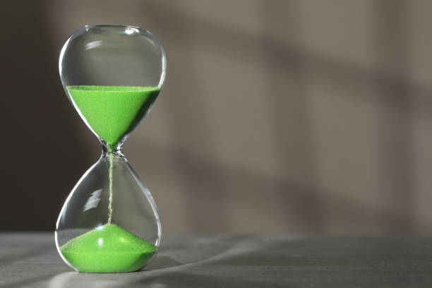 istock Hourglass with green flowing sand on table against light grey background, space for text 1911046337