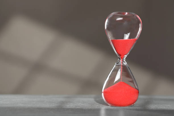 istock Hourglass with red flowing sand on table against light grey background, space for text 1911047965