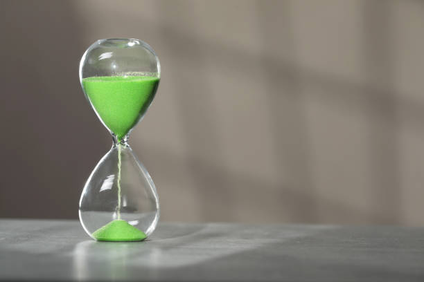 istock Hourglass with green flowing sand on table against light grey background, space for text 1911047967