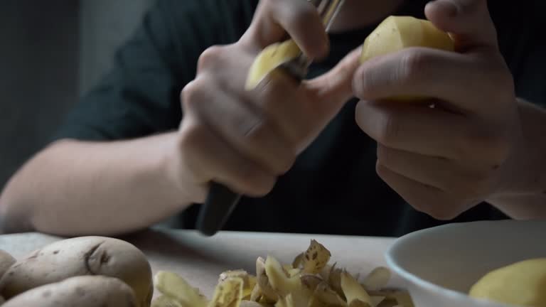 Men's hands peel potatoes at the kitchen table. A cinematic picture.