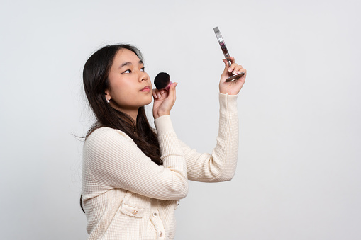 Beautiful young woman makes blush on her face using makeup brush on isolated white background. Teenage girl doing her own makeup. Close up portrait. Copy, empty space for text