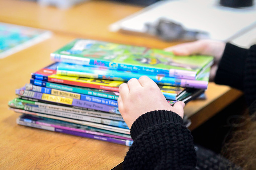 Image of a librarian's hands as she sorts through a pile of children's books that are out of focus. Children's books have been a focus of book bans across the United States.