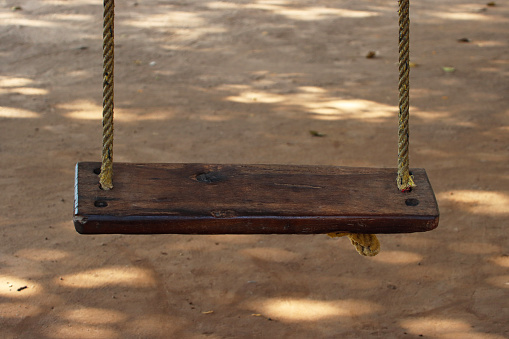 Stock photo showing close-up of a woodland swing tied to the branch of a tree by rope in dappled sunlight.