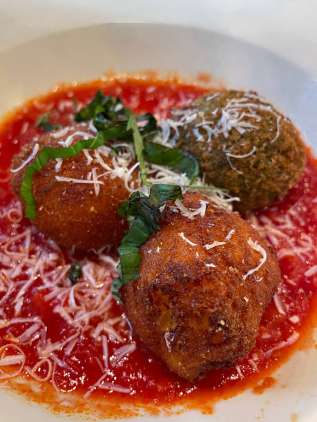 istock Full frame image of white bowl containing three, arancini rice balls (rice croquettes) served with tomato sauce and topped with grated parmesan cheese, elevated view 1911227093