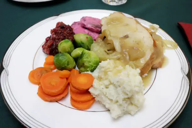 Plate full of Christmas dinner of mashed potatoes, carrots, brussels sprouts, homemade chutney, beets with yogurt, turkey meat, gravy and onions. Round plate with a colorful Christmas dinner closeup