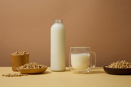 Front view of wooden dishes and bowl of soybeans displayed with bottle and glass of soy milk. Beige background. Concept of organic foods advertising
