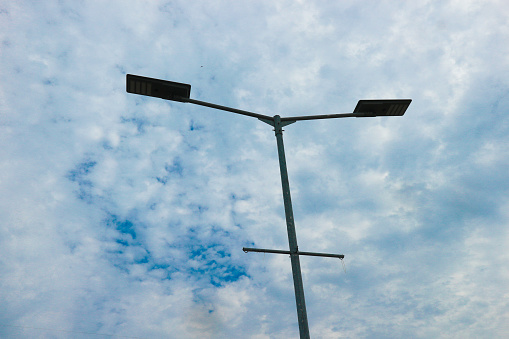 Street light pole close up shot, with blue sky with white clouds in the background.