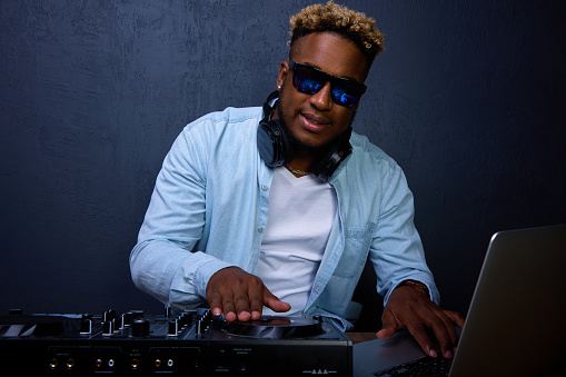 African-American DJ works in a studio with headphones, a mixer and other equipment. Enjoys his occupation. A black man DJ wearing sunglasses.