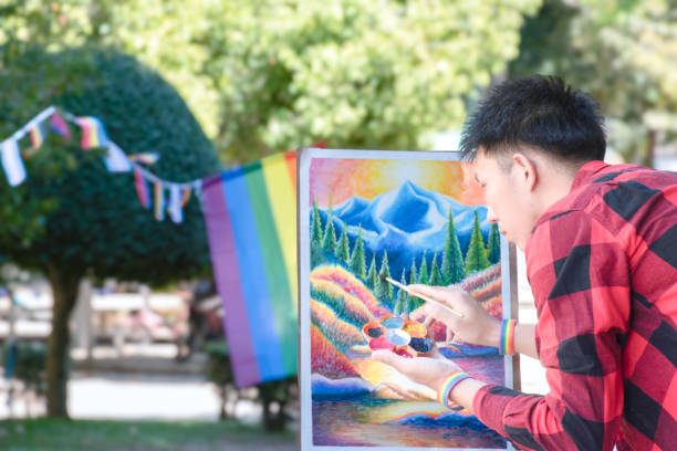 Asian boy in plaid shirt wears rainbow wristband and doing art painting, coloring, sketching and fixing his art in community park, soft focus.