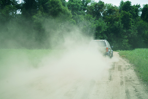 vehicle driving on dirt road with dust in air