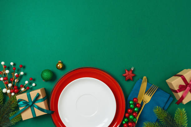 istock Christmas table decoration with plate, gift box and ornaments on green background. Elegant template for holiday card, invitation and design 1911361203