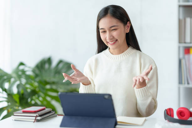 istock Beautiful young Asian woman college student is video chatting with her classmates using laptop, smiling faces and gestures happily studying. 1911393743