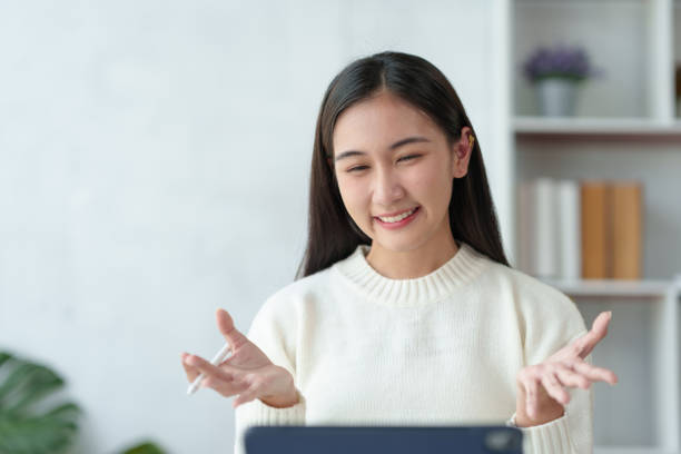 istock Beautiful young Asian woman college student is video chatting with her classmates using laptop, smiling faces and gestures happily studying. 1911393746