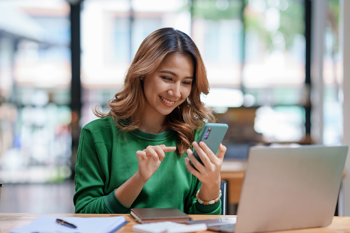 Beautiful Asian woman using smartphone to check work contact customers, answer chats, complete transactions and use social media application.