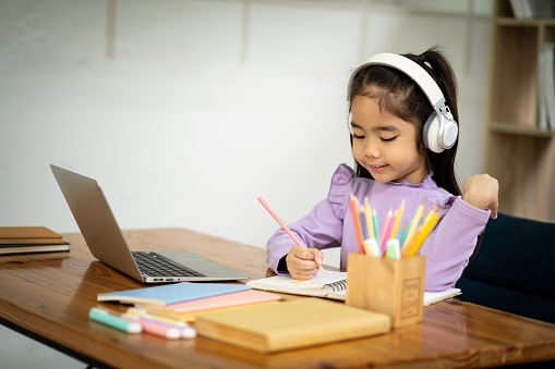Young Asian female student wearing headphones studying watching video conference, laptop computer, online distance learning at home