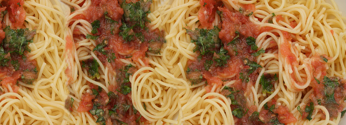Spaghetti with raw tomato sauce garnished with basil and garlic